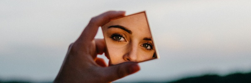 hand holding a square compact mirror, reflection of eyes