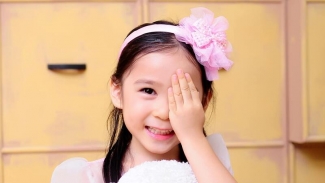 young girl, covering her left eye with her hand, standing in front of a yellow background