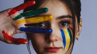woman with primary colour streaks in her face and on her hand which covers half the face