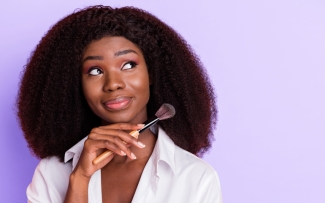 woman with a make up brush in hand purple background