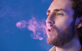 man exhaling cigarette smoke on purplish background