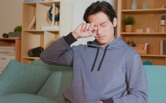 Man sitting on couch rubbing eye irritation