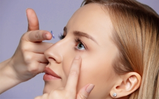 blonde woman inserting a contact lens into her left eye