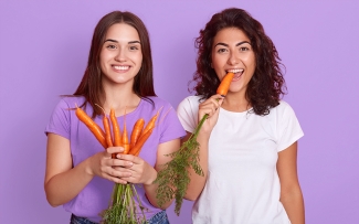 two girls eating carrots on purple background