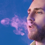 man exhaling cigarette smoke on purplish background
